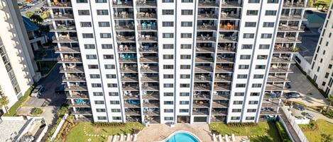 A high-rise building with multiple balconies, a swimming pool, and a parking area.