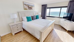 A bedroom with a large bed, a nightstand with a lamp, a dresser, and a TV.