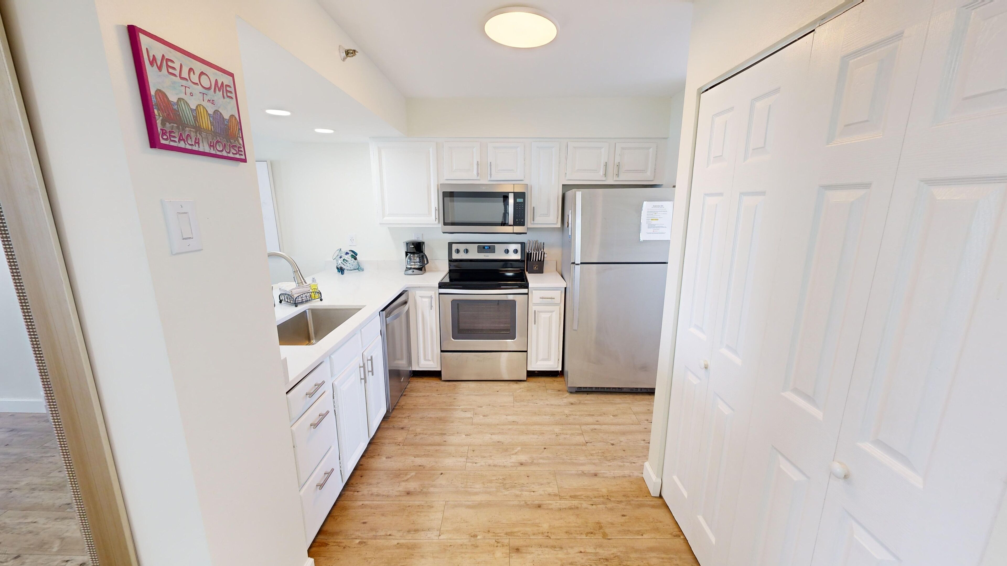 A compact kitchen with white cabinets, a stainless steel refrigerator, an oven, and a microwave.