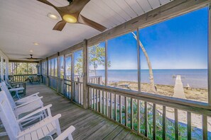 A covered porch with white chairs, a wooden deck, and a view of the beach. - Bayside Bungalow 9531 3 Bedroom Home (Gulf Shores)