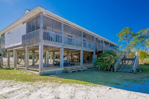 A two-story beach house with a balcony, outdoor seating, and a staircase leading to the upper level. - Bayside Bungalow 9531 3 Bedroom Home (Gulf Shores)