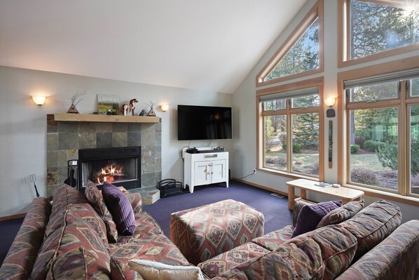 Una sala de estar acogedora con chimenea de piedra, televisor de pantalla plana y un amplio ventanal con vistas al exterior.