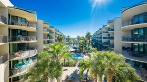 A resort with multiple balconies, a central pool, and palm trees. - Phoenix On The Bay 1419 2 Bedroom Condo (Orange Beach)