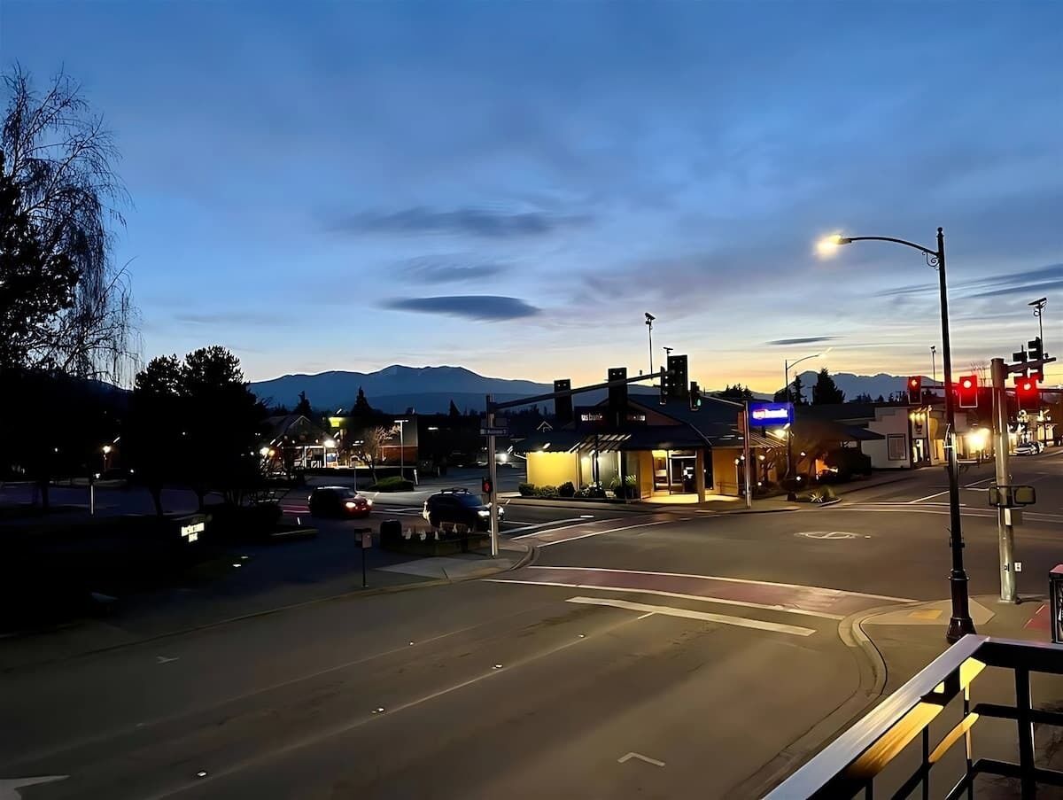 A street view at dusk with a crosswalk, traffic lights, and a building with illuminated signage.