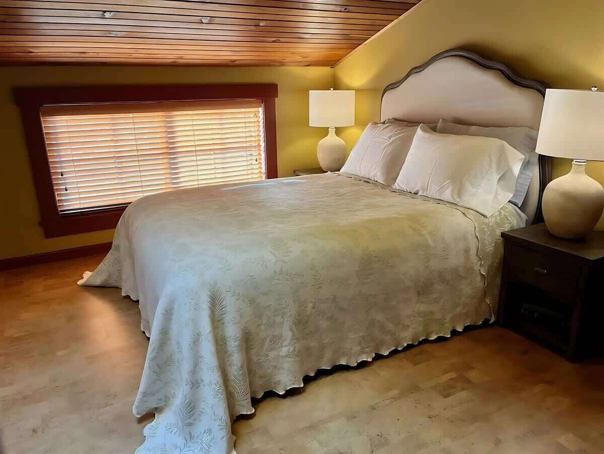 Ein Schlafzimmer mit einem Bett, zwei Nachttischlampen, einem Nachttisch und einem Fenster mit Jalousien.