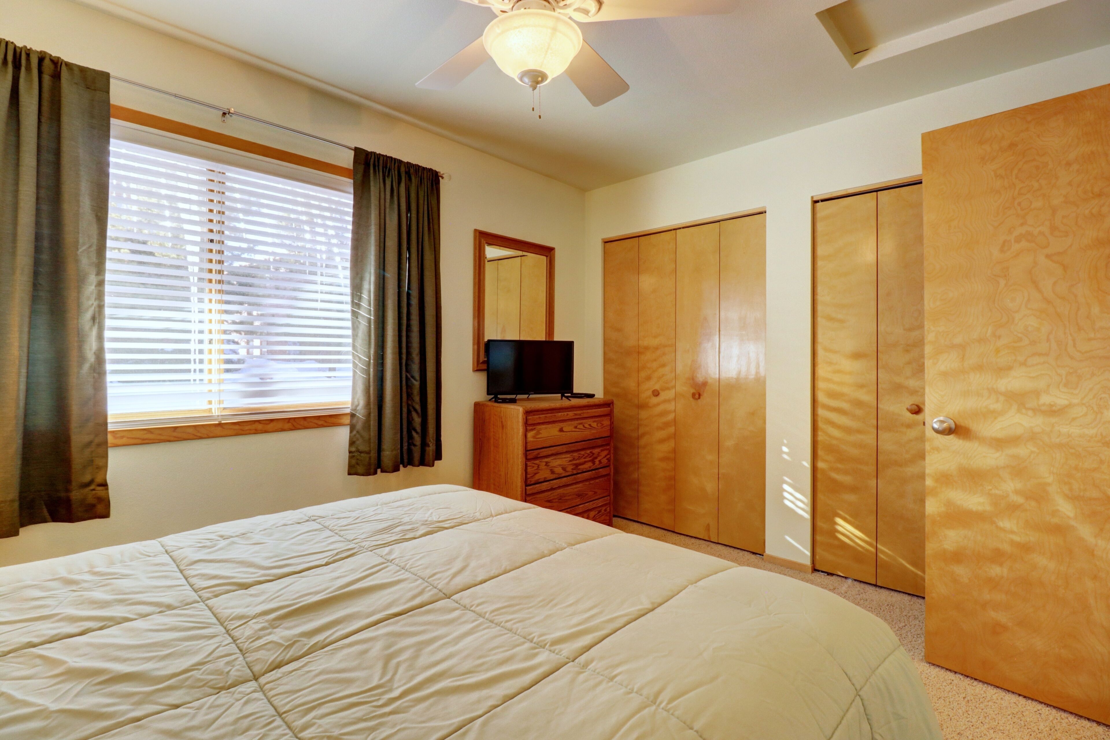 A bedroom with a bed, a dresser, a television, and wooden wardrobes.