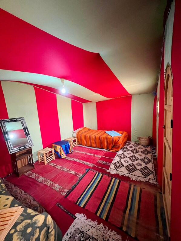 A bedroom with a bed, a small table, a mirror, and a red and white striped wall. - Bivouak Mhamid (M'Hamid El Ghizlane)