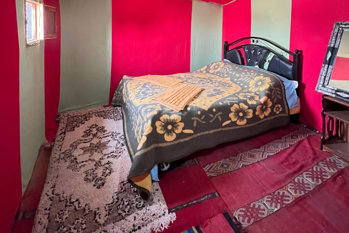 A bedroom with a bed, a nightstand, a mirror, and a window.
