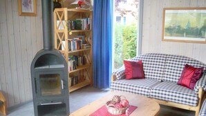 Un salon chaleureux avec un canapé à carreaux, une table en bois sur laquelle est posé un panier, une bibliothèque et un poêle à bois.
