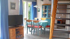 Une pièce comprenant un téléviseur posé sur un meuble en bois, une table à manger avec des chaises, et un buffet bleu aux portes vitrées.