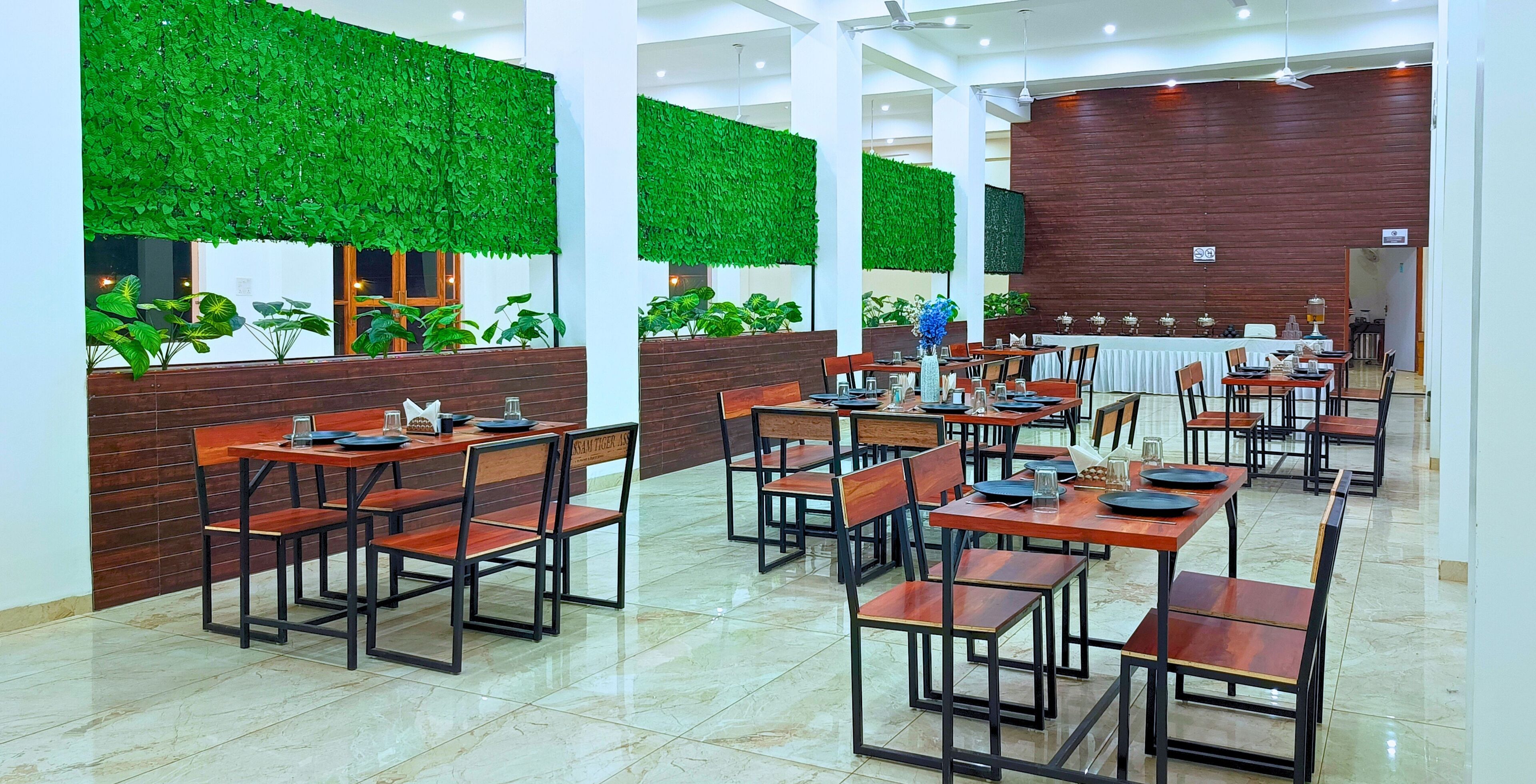 A restaurant with multiple tables and chairs, green wall decorations, and a wooden accent wall.