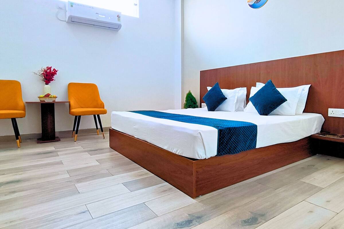 Ein Hotelzimmer mit einem hölzernen Bett, zwei orangefarbenen Sesseln, einem kleinen Tisch mit einer Vase und einer Topfpflanze.