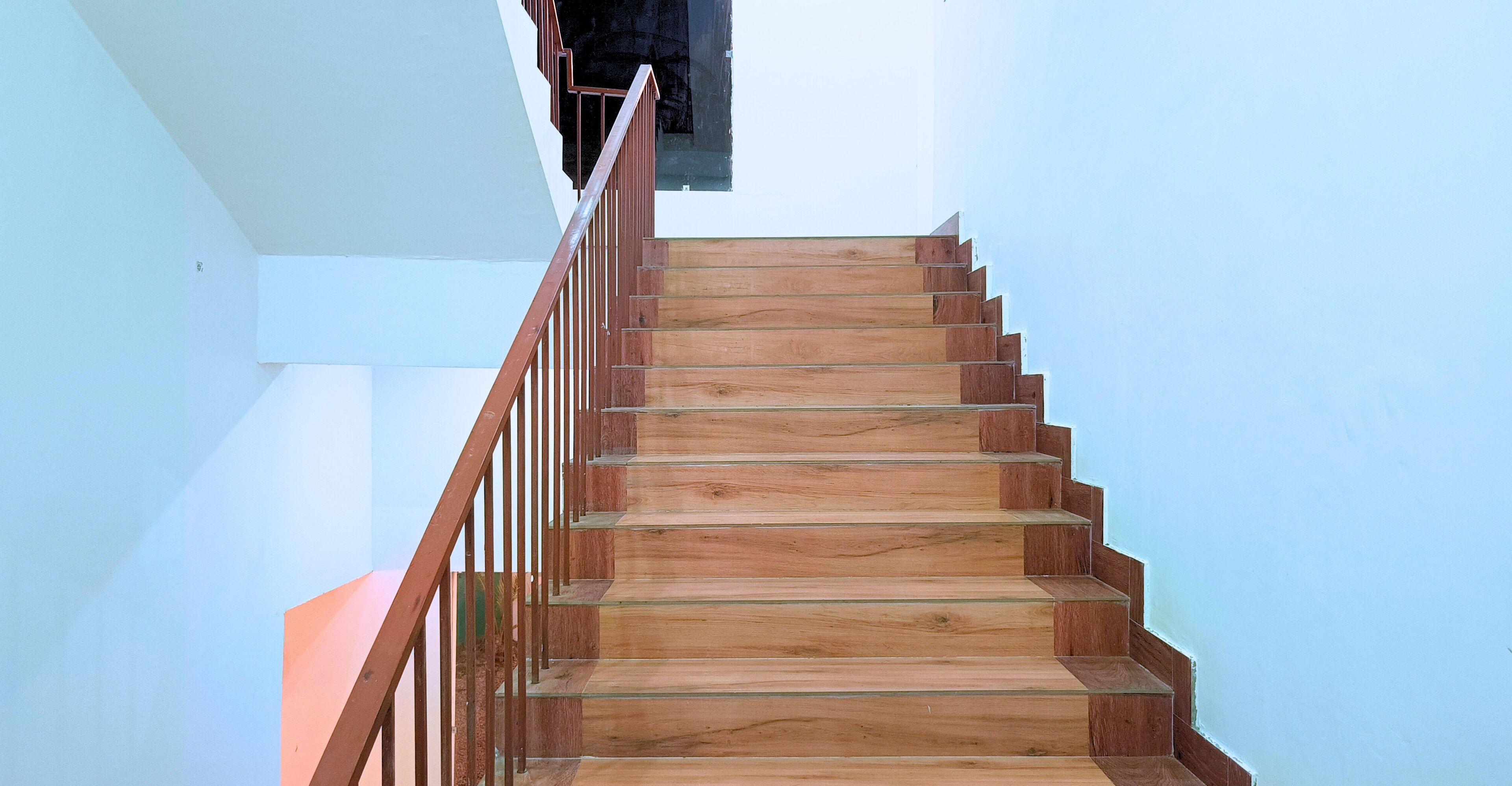 A wooden staircase with a metal handrail, leading to an upper floor.