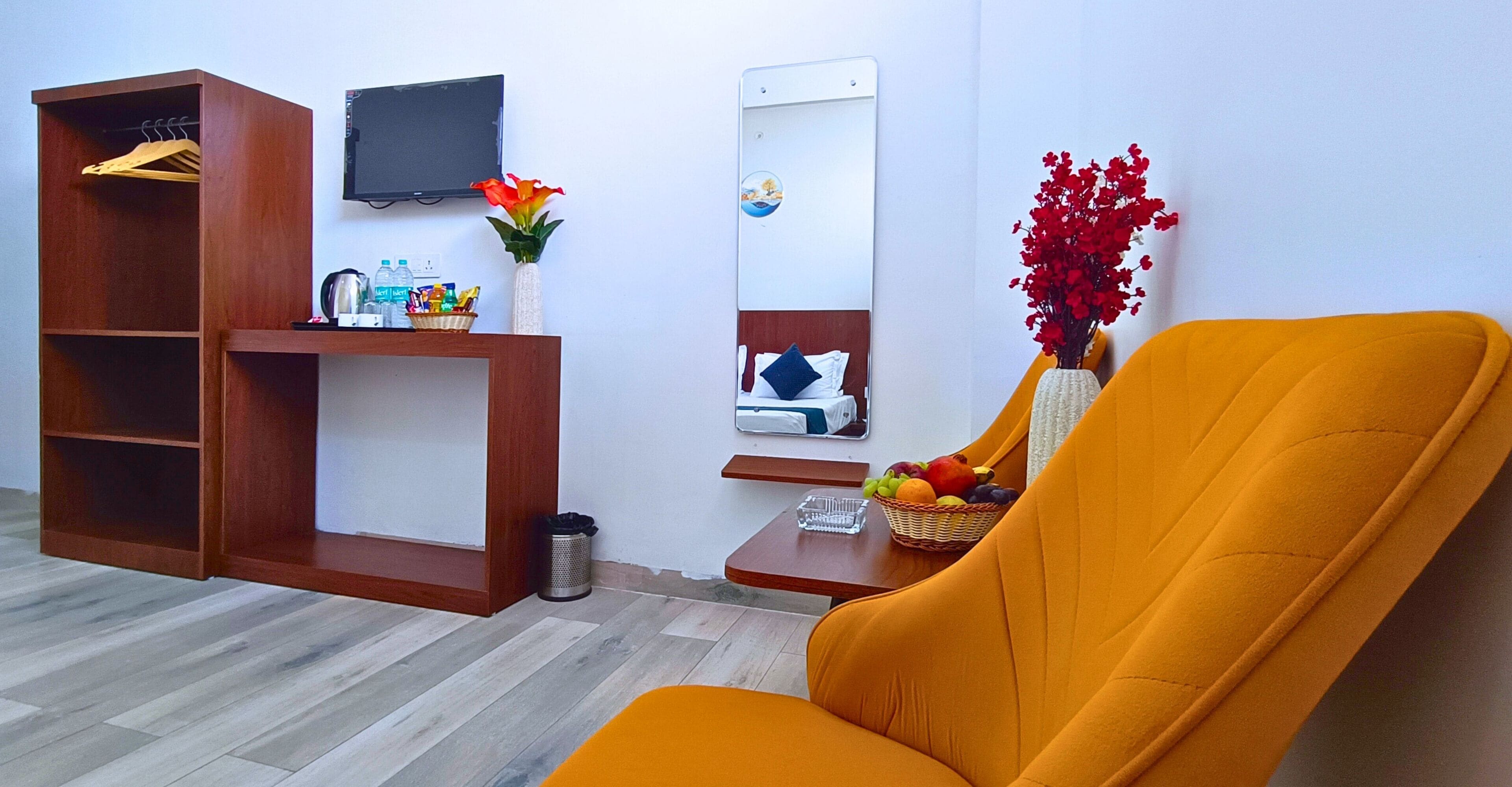 Habitación de hotel con armario de madera, una mesita con artículos de aseo, una cesta de frutas, un espejo y un televisor.