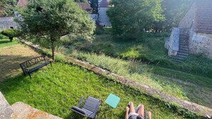 A grassy outdoor area with a stone bench, a small table, and a person lying on a lounge chair.