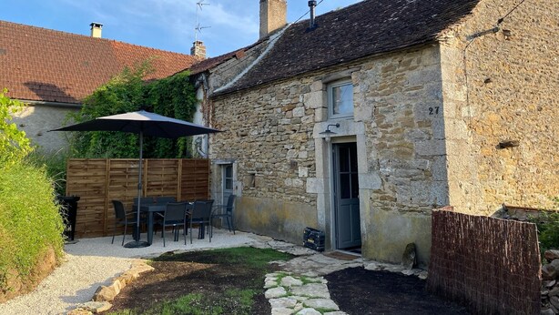A stone house with a tiled roof, a wooden fence, and a gravel patio with a table and chairs.