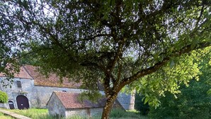 A bench in a grassy area with a tree and a stone building in the background.