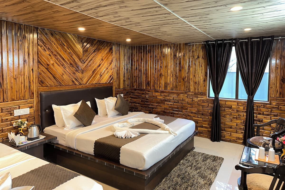 Una camera d'albergo con un letto grande, pareti con pannelli in legno, una finestra con tende e un tavolino con un vaso e delle candele.