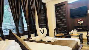 A hotel room with a bed, a chair, a small table, a TV, and a window with curtains.