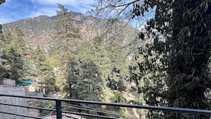A balcony with a view of a mountainous landscape, a river, and a small building in the distance.