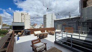 A rooftop terrace with wooden furniture, string lights, and a view of surrounding buildings. - Hotel Vida (Puerto Madryn)