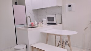 A modern kitchen with white cabinetry, a microwave, a sink, and a small dining table with benches. - 5sec dongmyo station apartment (Seoul)