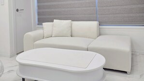 A modern living room with a white sofa, a white coffee table, and a window with horizontal blinds. - 5sec dongmyo station apartment (Seoul)
