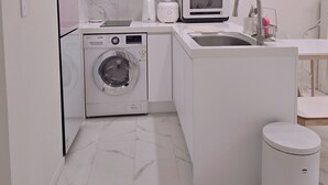 A compact kitchen with a washing machine, microwave, sink, and a trash bin. - 5sec dongmyo station apartment (Seoul)