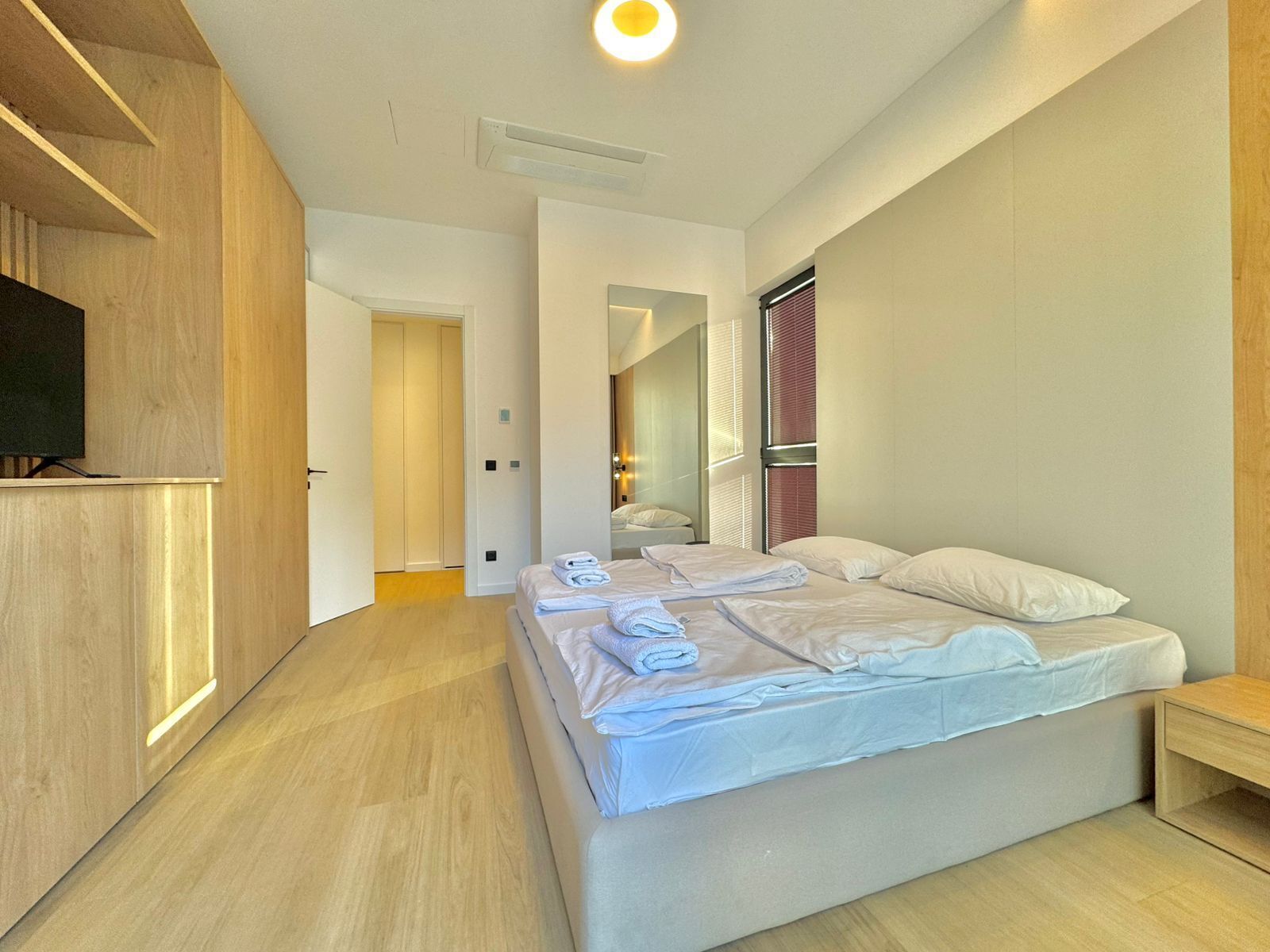 Une chambre d’hôtel moderne avec un grand lit, un téléviseur posé sur un meuble en bois et un dressing.