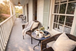 Eine Veranda mit Korbmöbeln, zwei weiße Kaffeetassen, ein Buch und ein kleiner Topfpflanze.