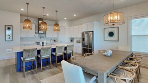 A modern kitchen with white cabinets, a stainless steel refrigerator, and a dining area with a wooden table and chairs.