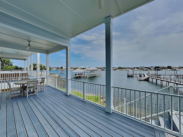 A covered deck with a view of a marina and houses in the distance.