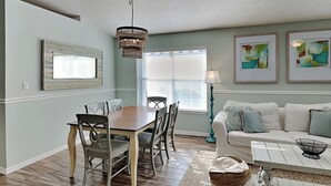 A dining area with a wooden table and chairs, a chandelier, and a window with blinds. - Emerald Port of Call | Luxe Home, Near Beach (Miramar Beach)