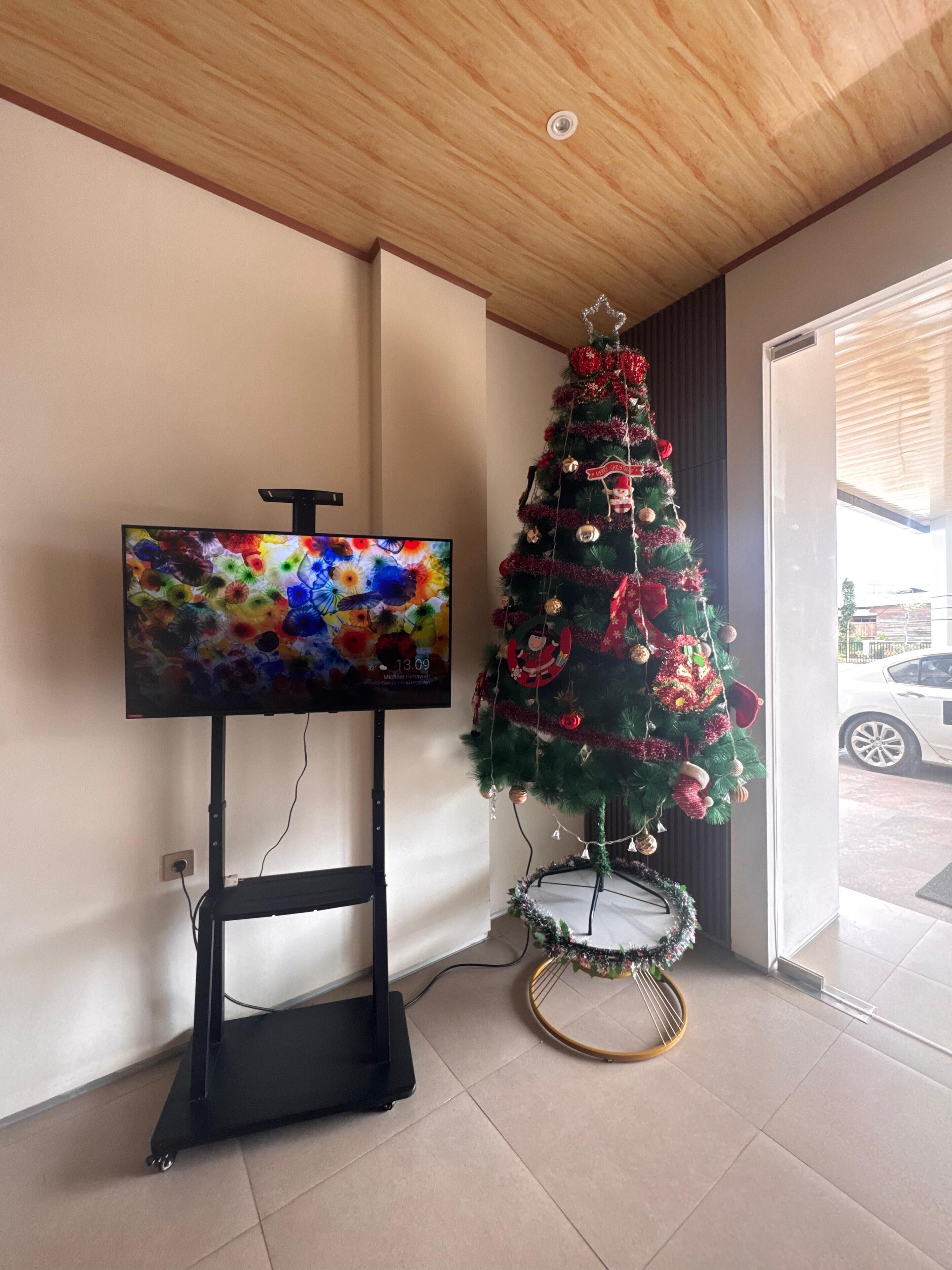 Um interior moderno com televisão de tela plana em um suporte, uma árvore de Natal decorada e vista da rua por uma porta de vidro.