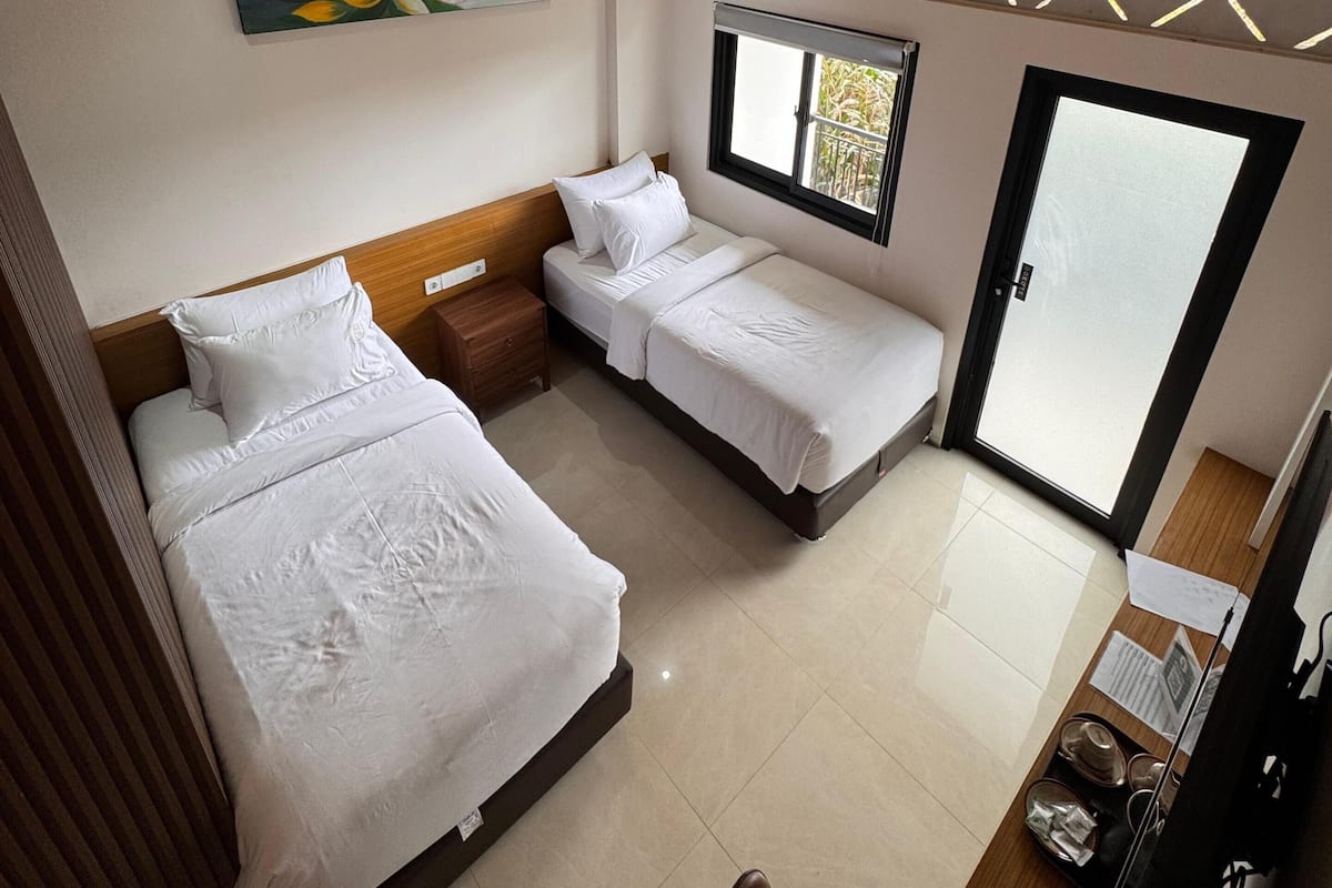 A hotel room with two beds, a painting, a window, and a door.