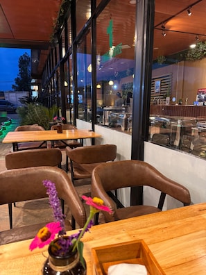 A restaurant with wooden tables and chairs, a view of the street, and a sign for Tong's Coffee. - ABE HOTEL & CONVENTION (Siborongborong)