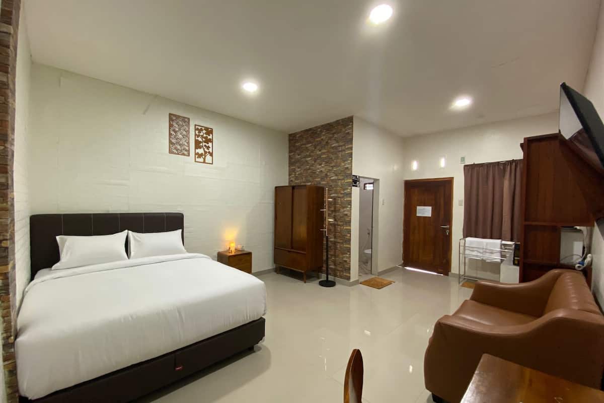 A hotel room with a large bed, a wooden wardrobe, a bathroom with a shower, and a seating area with a table and chairs.