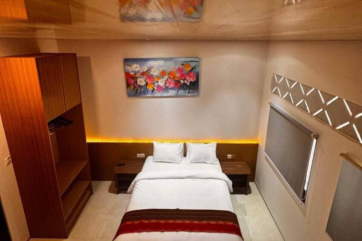 A modern bedroom with a bed, a nightstand, a TV, and a painting on the wall.