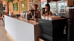 A modern coffee shop counter with a wooden finish, a coffee machine, and a display of coffee beans. - ABE HOTEL & CONVENTION (Siborongborong)