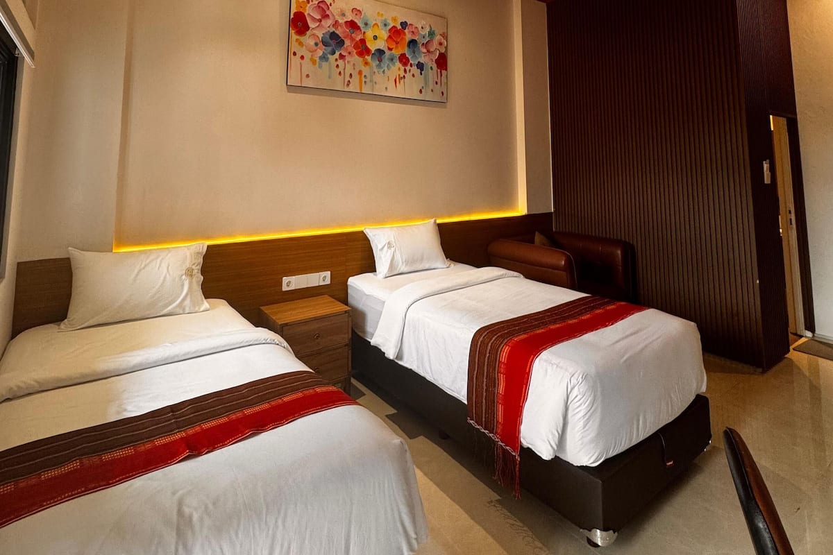 A hotel room with two beds, wooden ceiling, and a colorful artwork on the wall.