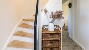 Eine Treppe mit Holzsitzen und einer weißen Wand. Auf einem Korbwannen befindet sich eine weiße Vase mit getrockneten Blumen.