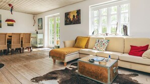 Ein geräumiges Wohnzimmer mit Holzboden, einem beigen Sofa, einem Couchtisch und einem großen Fenster mit Blick auf Grünflächen.