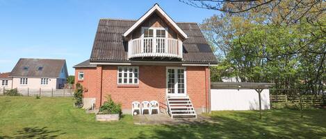 A two-story brick house with a balcony, a small front yard, and a neighboring house.
