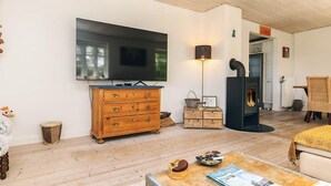 Ein gemütliches Wohnzimmer mit Holzboden, einem großen Flachbildfernseher, einer hölzernen Kommode, einem kleinen Tisch mit Zeitschrift und Gläsern sowie einem Kamin.