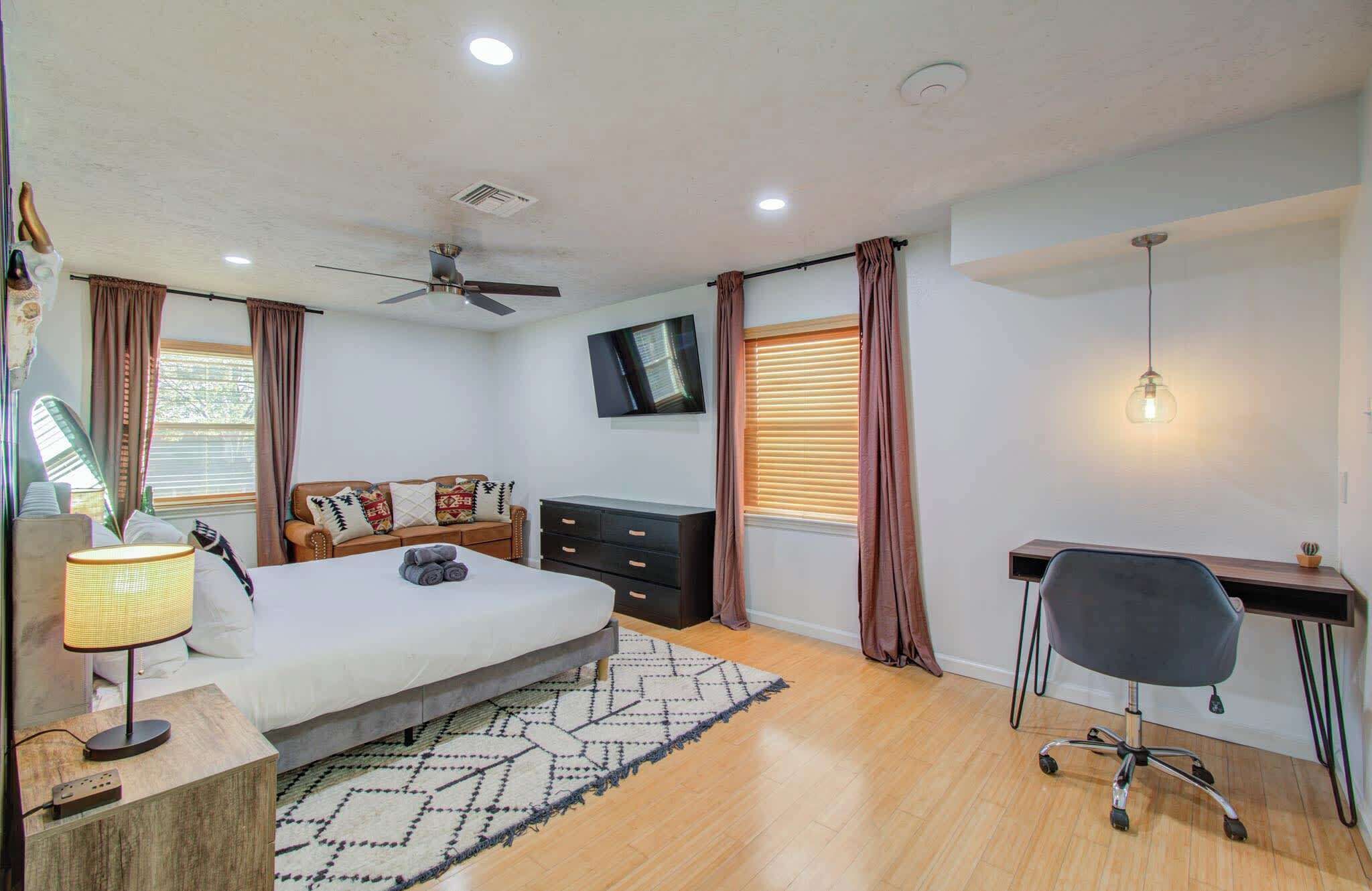 Un dormitorio moderno con cama, escritorio, silla, televisor y ventilador de techo.