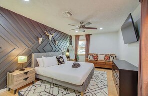 Un dormitorio con cama, mesitas de noche, ventilador de techo, televisor y una alfombra estampada.