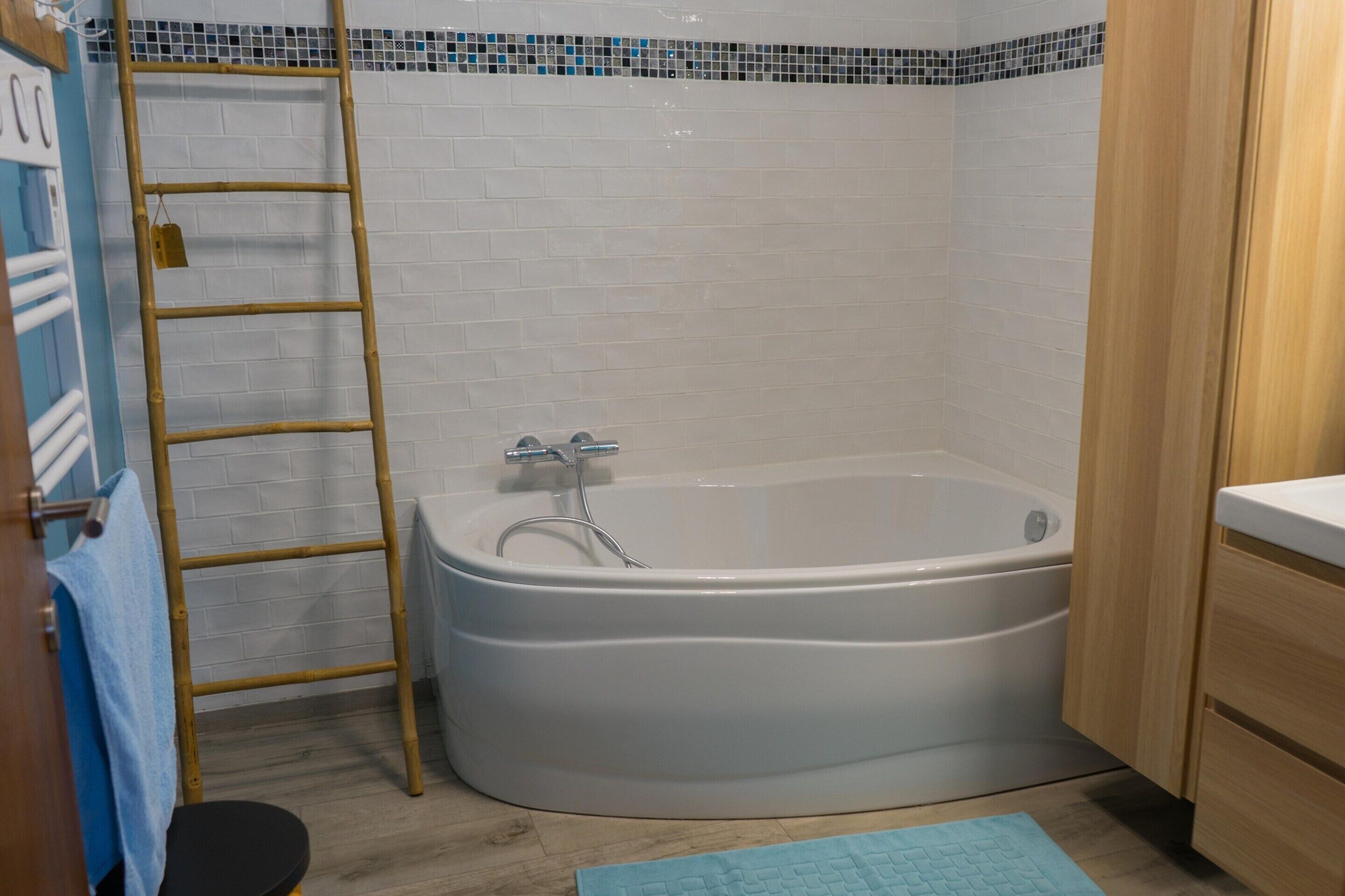 Un baño con una bañera blanca, una escalera de madera y una toalla azul en un perchero.