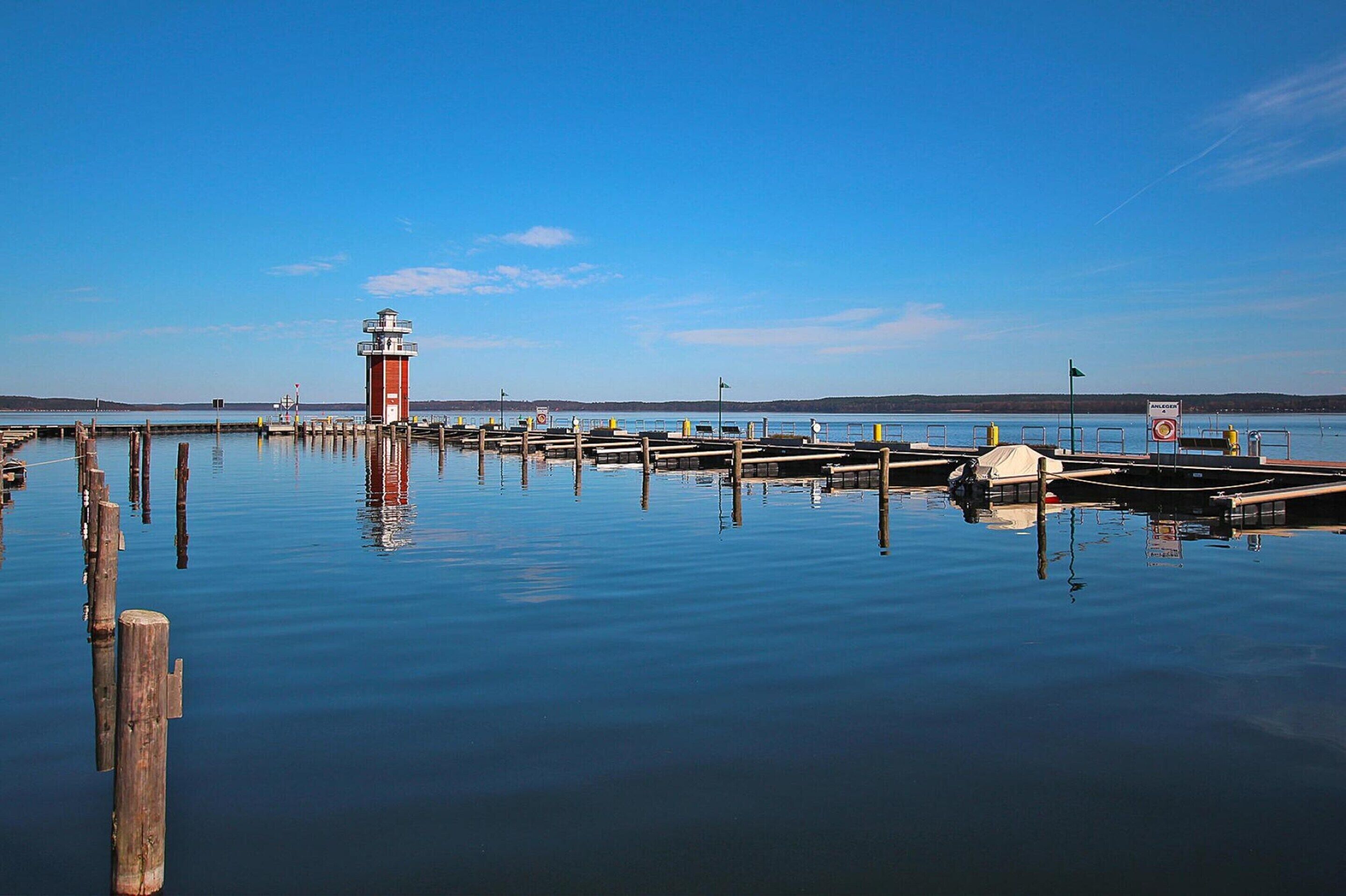 A calm waterfront with a lighthouse, wooden docks, and a clear blue sky.