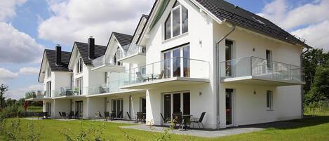 Une maison moderne à deux étages, dotée d’un balcon, d’une terrasse couverte et d’une pelouse bien entretenue.