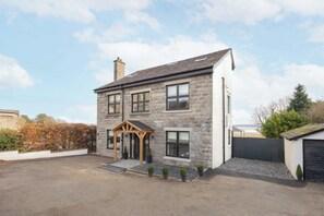 A two-story stone house with a wooden porch, a garage, and a gravel driveway. - Host & Stay | Bay View House (Grange-over-Sands)